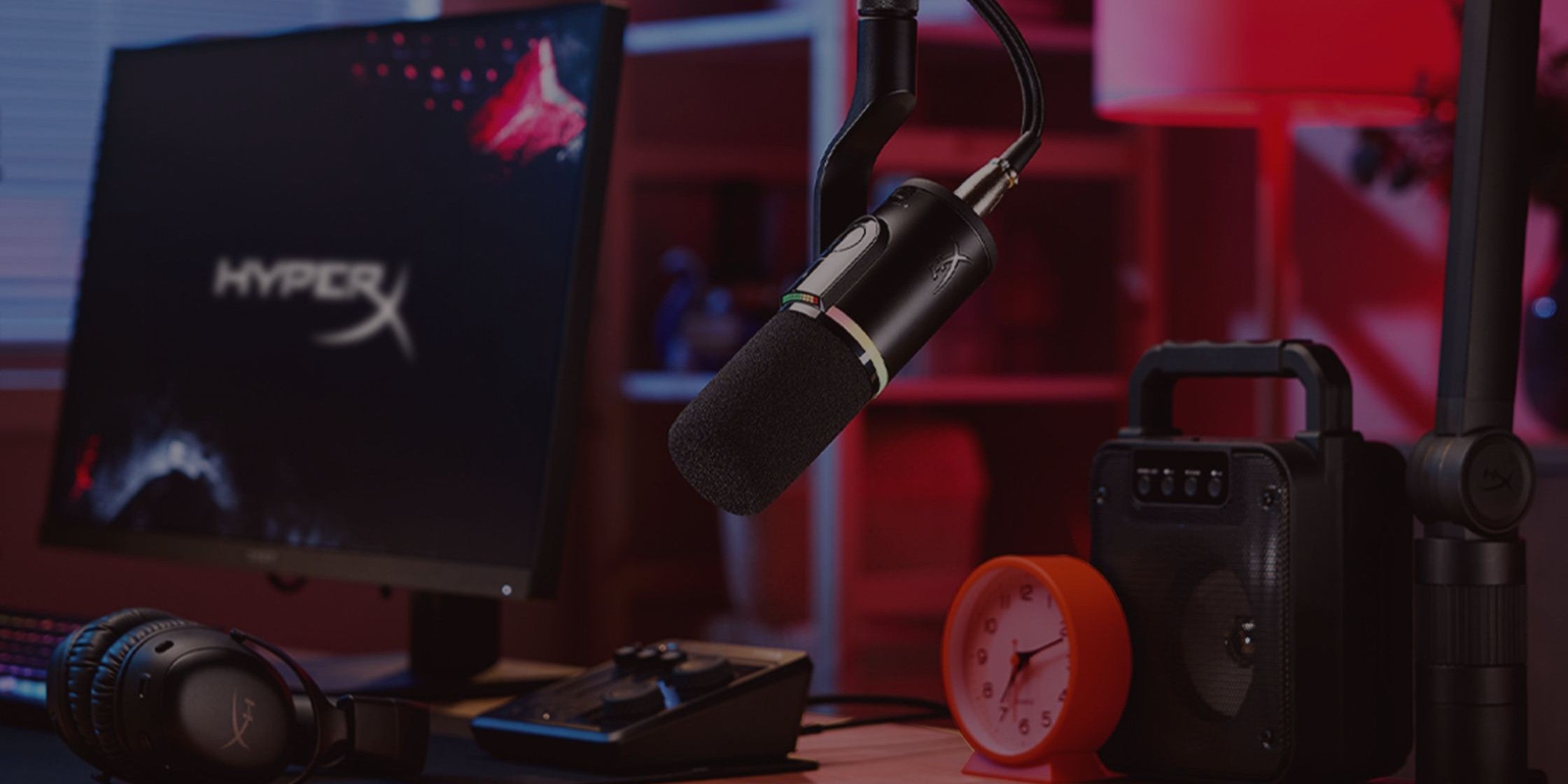 Configuration de jeu avec moniteur HyperX, microphone et haut-parleurs sur un bureau.
