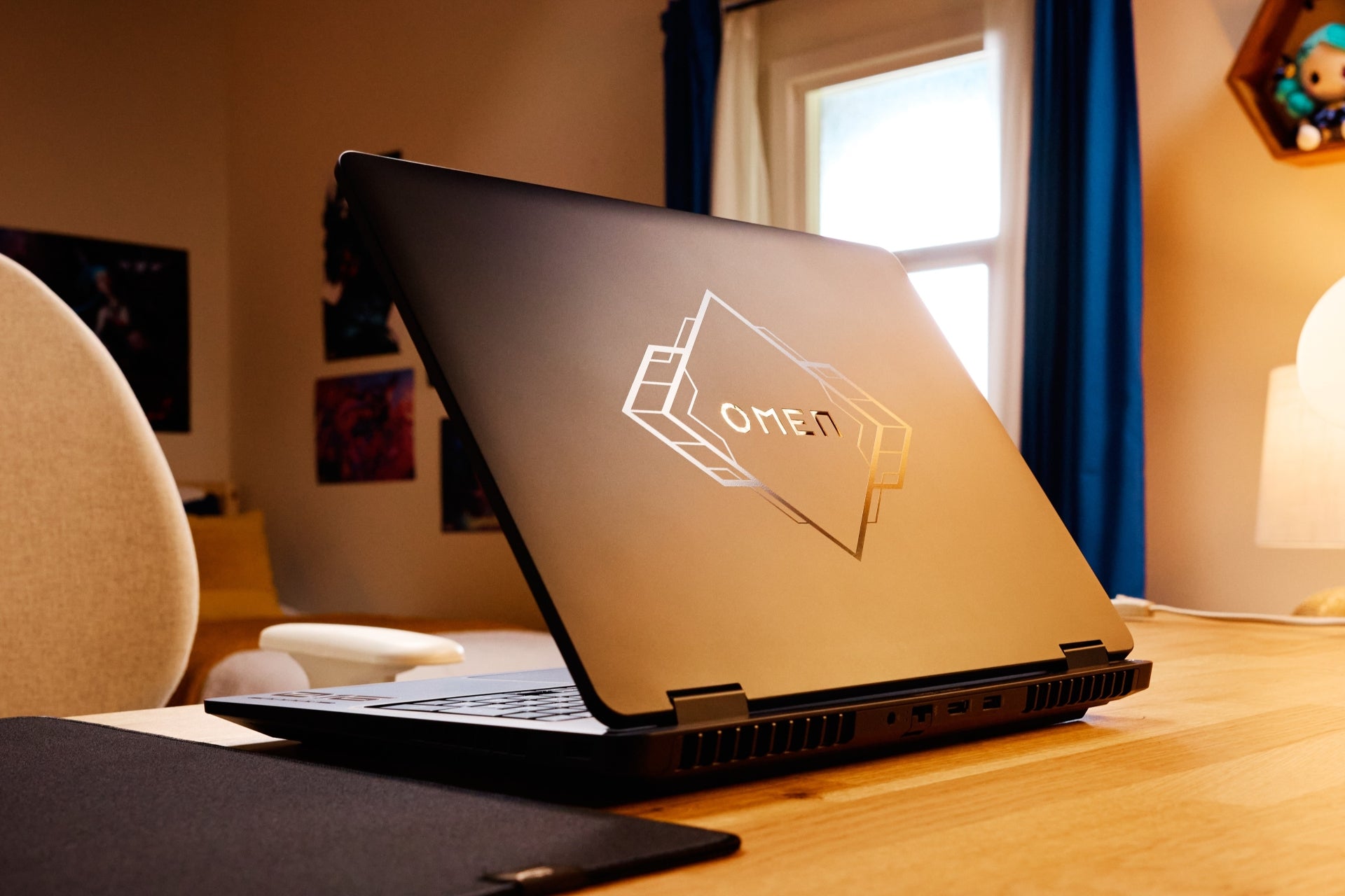 Ordinateur portable OMEN avec des accents dorés sur un bureau dans une pièce avec une fenêtre et une chaise.